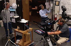 A single HD camera with teleprompter, a light panel, a floor director. some lights, and an SD field monitor.